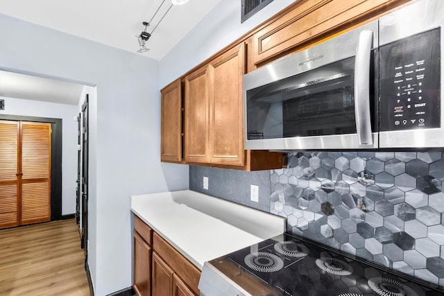 3103 Wycliff Ave, Dallas, TX 75219 - kitchen with stainless steel microwave, range, brown cabinetry, backsplash, and light wood finished floors