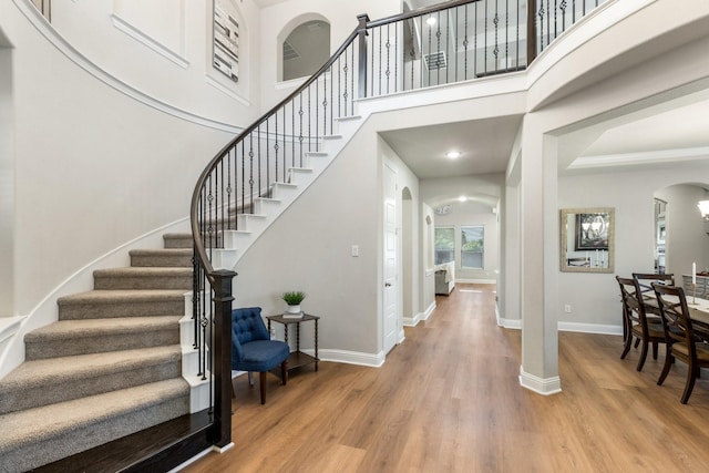 entrance foyer featuring arched walkways, light wood finished floors, baseboards, stairway, and a high ceiling