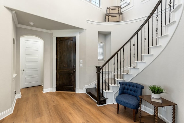 entrance foyer featuring wood finished floors, stairway, ornamental molding, baseboards, and arched walkways