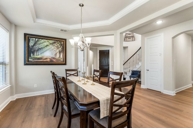 dining area featuring a raised ceiling, wood finished floors, stairs, baseboards, and a chandelier