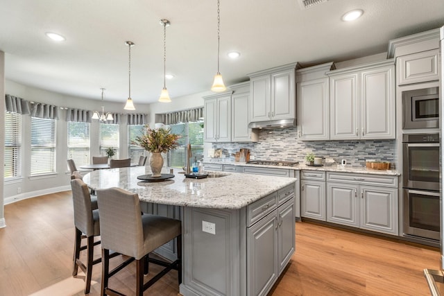 kitchen with gray cabinetry, a sink, stainless steel appliances, a kitchen island, and backsplash