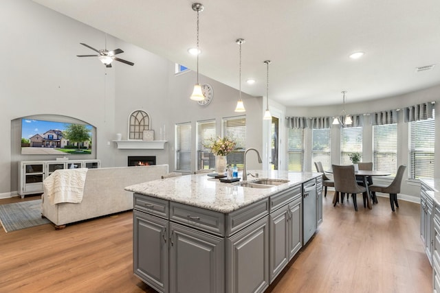 kitchen featuring gray cabinetry, a sink, stainless steel dishwasher, light wood-style flooring, and open floor plan