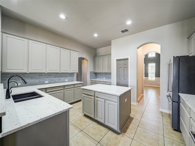 kitchen featuring a sink, arched walkways, freestanding refrigerator, gray cabinetry, and recessed lighting