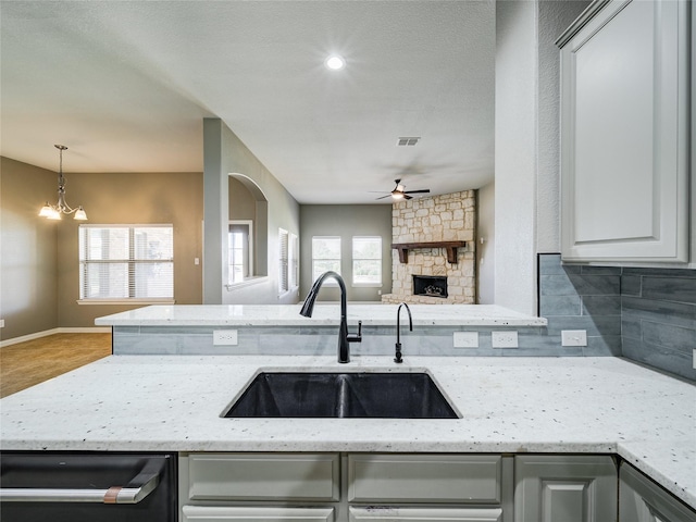 kitchen featuring a sink, open floor plan, a ceiling fan, a fireplace, and light stone countertops