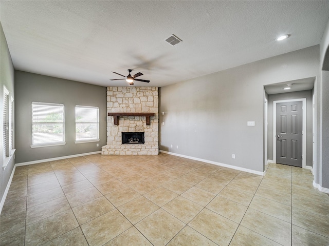 unfurnished living room featuring a ceiling fan, light tile patterned floors, a textured ceiling, a stone fireplace, and baseboards