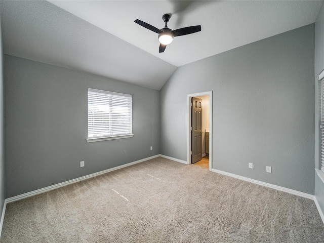unfurnished bedroom with light colored carpet, lofted ceiling, baseboards, ensuite bath, and ceiling fan
