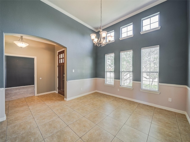 unfurnished room featuring arched walkways, light tile patterned flooring, healthy amount of natural light, crown molding, and a chandelier