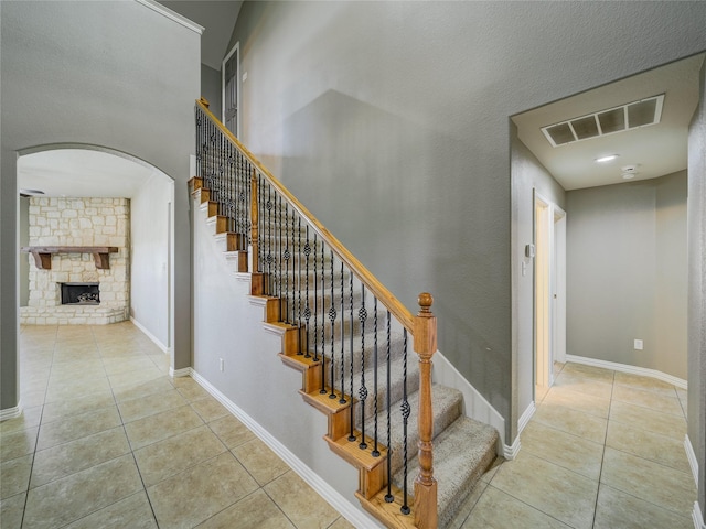 stairway featuring tile patterned floors, arched walkways, a stone fireplace, and baseboards