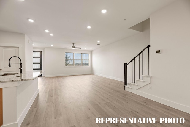 unfurnished living room with a sink, ceiling fan, light wood-style floors, recessed lighting, and baseboards