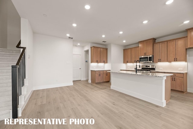 kitchen with appliances with stainless steel finishes, light wood-style flooring, recessed lighting, brown cabinets, and a kitchen island with sink