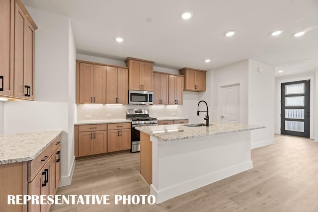 kitchen with appliances with stainless steel finishes, a sink, light wood-style flooring, tasteful backsplash, and an island with sink