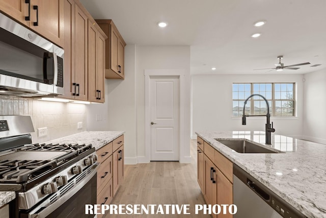 kitchen featuring stainless steel appliances, a sink, light wood finished floors, tasteful backsplash, and ceiling fan