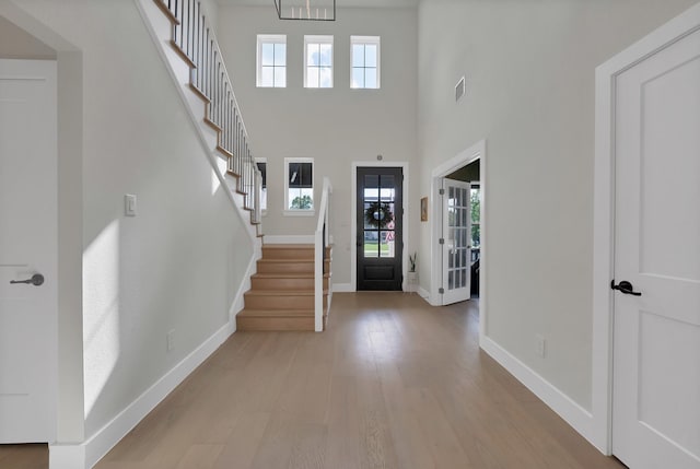 foyer featuring light wood-type flooring, stairway, baseboards, a high ceiling, and a chandelier