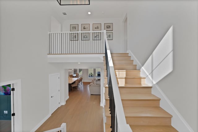 staircase with wood finished floors, a high ceiling, baseboards, and recessed lighting