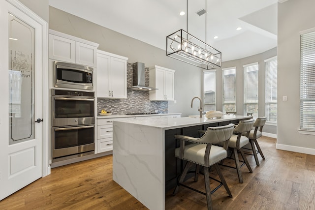 2831 Sheffield Ct, Trophy Club, TX 76262 - kitchen featuring wall chimney range hood, appliances with stainless steel finishes, a kitchen island with sink, backsplash, and white cabinetry