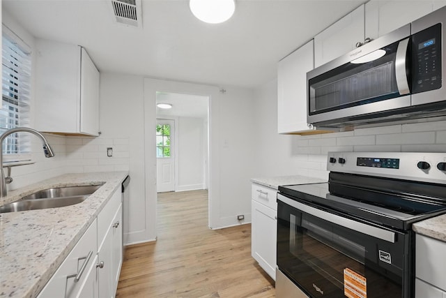 kitchen with stainless steel appliances, a sink, light wood-style floors, tasteful backsplash, and white cabinetry