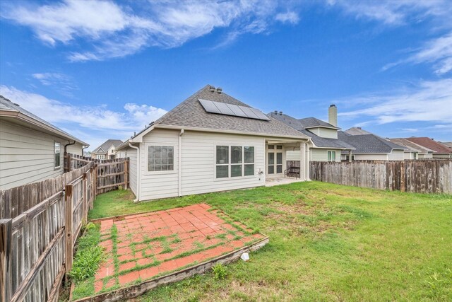 rear view of property featuring a patio, solar panels, and a shingled roof