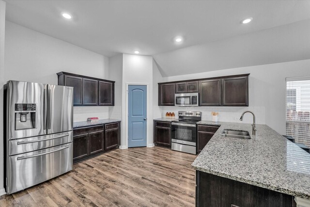 kitchen featuring stainless steel appliances, a sink, light stone counters, dark brown cabinets, and light wood finished floors