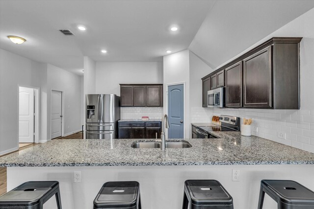 kitchen with appliances with stainless steel finishes, a sink, dark brown cabinets, light stone counters, and recessed lighting