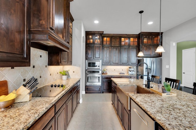 102 Willowbrook Dr, Waxahachie, TX 75165 - kitchen featuring appliances with stainless steel finishes, a sink, decorative light fixtures, dark brown cabinetry, and light stone countertops