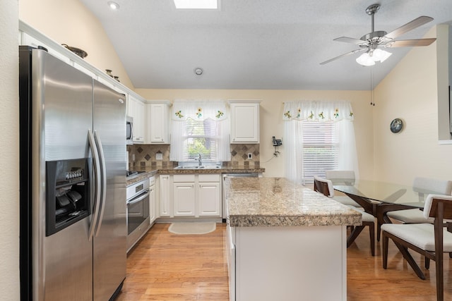 kitchen featuring stainless steel appliances, vaulted ceiling, a sink, light wood-type flooring, and a center island