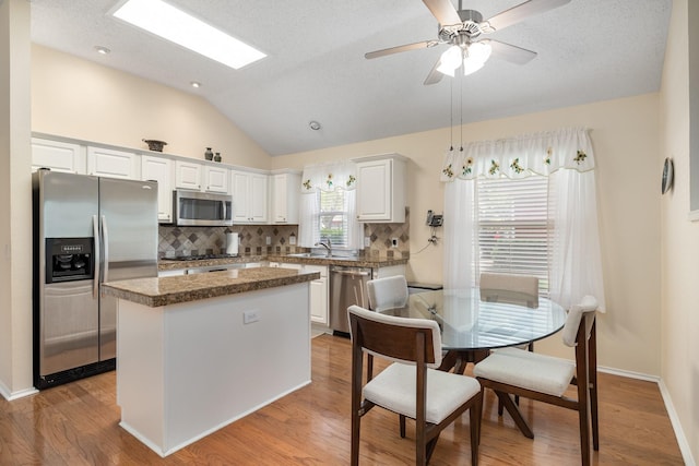 kitchen featuring appliances with stainless steel finishes, a center island, lofted ceiling, decorative backsplash, and white cabinets