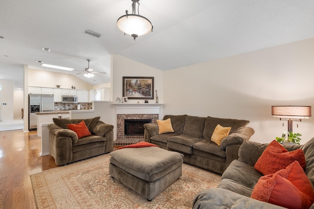 living area featuring light wood-style flooring, a ceiling fan, vaulted ceiling, and a fireplace