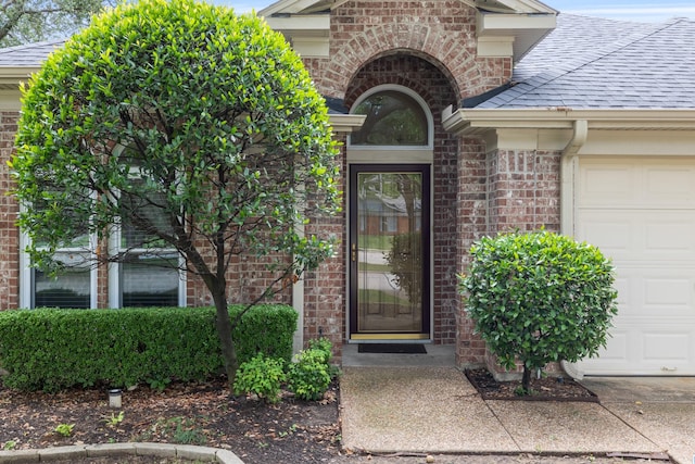 doorway to property with a garage, brick siding, and a shingled roof