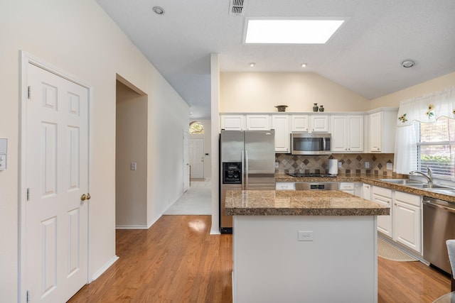 kitchen with stainless steel appliances, a sink, a center island, white cabinetry, and vaulted ceiling
