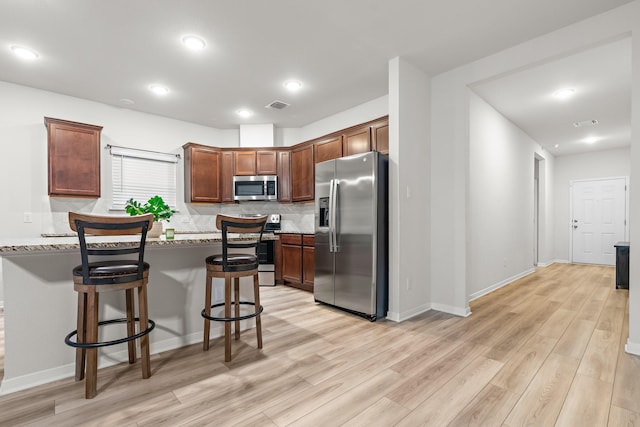 kitchen with stainless steel appliances, light wood-type flooring, a breakfast bar area, decorative backsplash, and recessed lighting