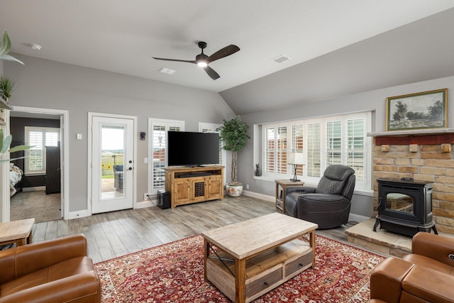 living area featuring a wood stove, a ceiling fan, wood finished floors, baseboards, and lofted ceiling