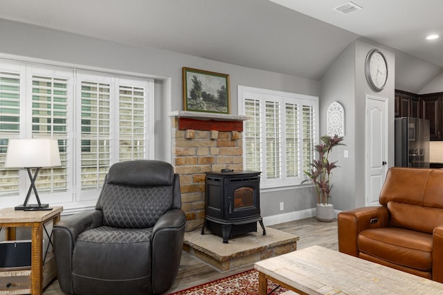 living area with a wood stove, light wood-style flooring, baseboards, and vaulted ceiling