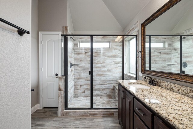full bathroom featuring vaulted ceiling, a stall shower, vanity, wood finished floors, and a textured wall