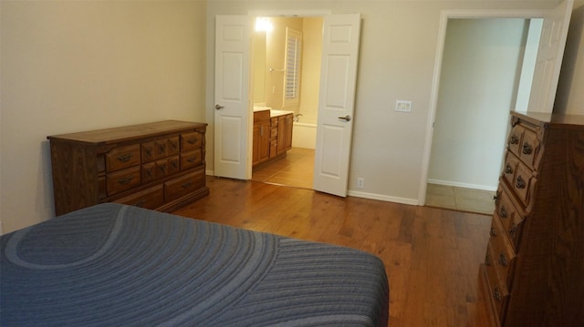 bedroom featuring wood finished floors, baseboards, and ensuite bath