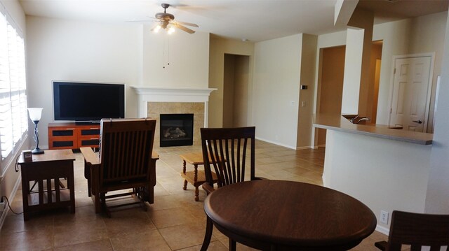 tiled living area with a ceiling fan, a tiled fireplace, and baseboards