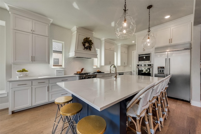 15102 Crape Myrtle Rd, Frisco, TX 75035 - kitchen featuring appliances with stainless steel finishes, light wood finished floors, a kitchen island with sink, premium range hood, and a kitchen breakfast bar