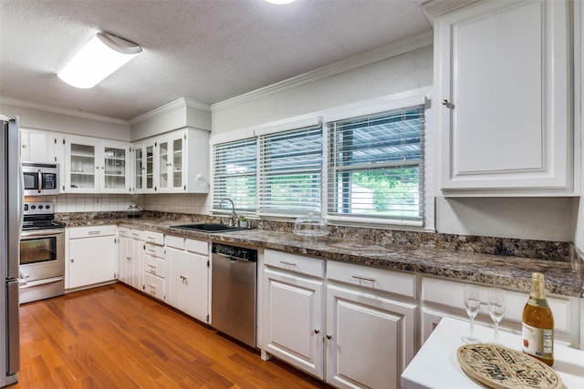 kitchen with stainless steel appliances, a sink, plenty of natural light, ornamental molding, and white cabinets