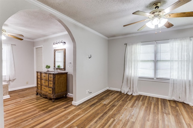 spare room with ceiling fan, arched walkways, wood finished floors, a textured ceiling, and baseboards