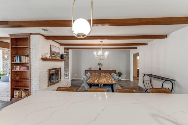 dining room with beam ceiling, a fireplace, a chandelier, baseboards, and wood finished floors