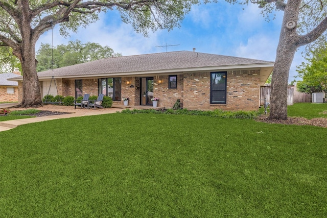 ranch-style home with a front lawn, brick siding, a shingled roof, and a patio