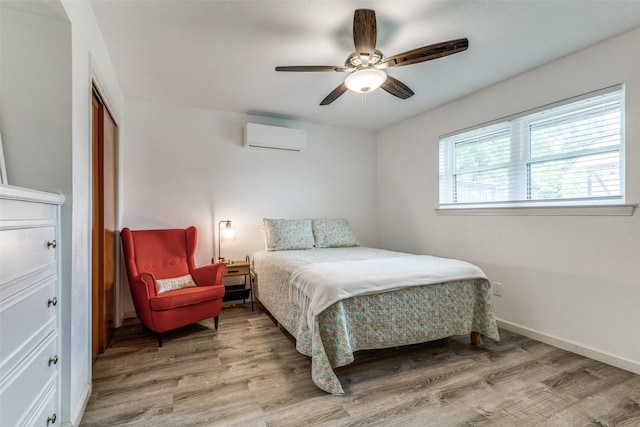 bedroom featuring an AC wall unit, light wood-style flooring, baseboards, a ceiling fan, and a closet