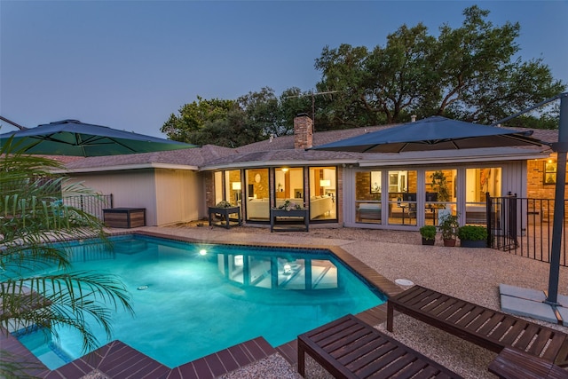 back of property with a chimney, an outdoor pool, a patio, and fence