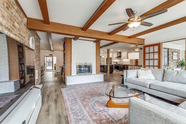 living room featuring a fireplace, ceiling fan, beamed ceiling, light wood-style floors, and brick wall