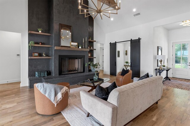 9001 Emma Ct, Granbury, TX 76049 - living room featuring a chandelier, a high ceiling, light wood-type flooring, a barn door, and a brick fireplace