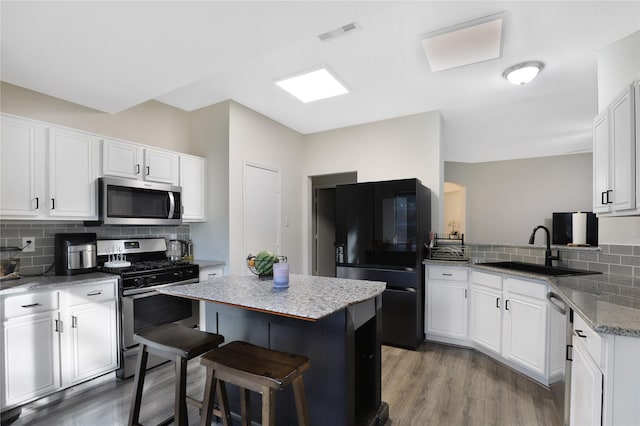 kitchen with appliances with stainless steel finishes, a sink, backsplash, a kitchen island, and light wood-style floors