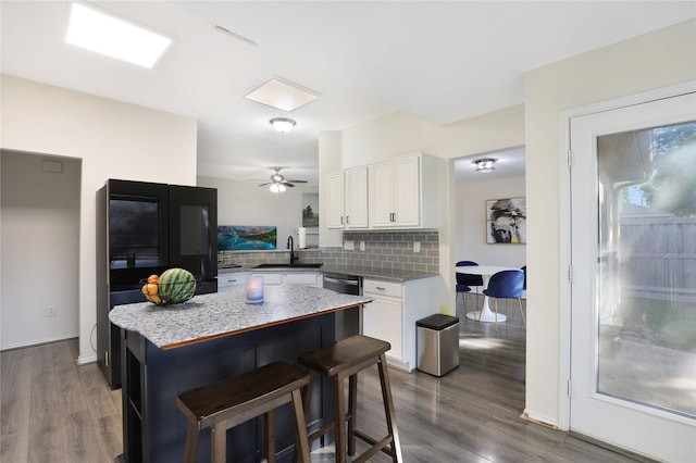 kitchen with a sink, white cabinets, wood finished floors, decorative backsplash, and a kitchen bar