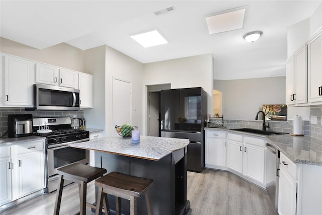 kitchen with stainless steel appliances, a sink, decorative backsplash, and white cabinetry