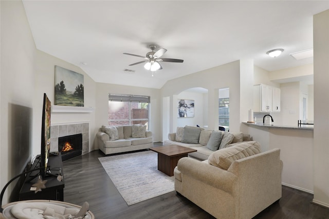 living area featuring ceiling fan, a fireplace, dark wood-style flooring, and arched walkways