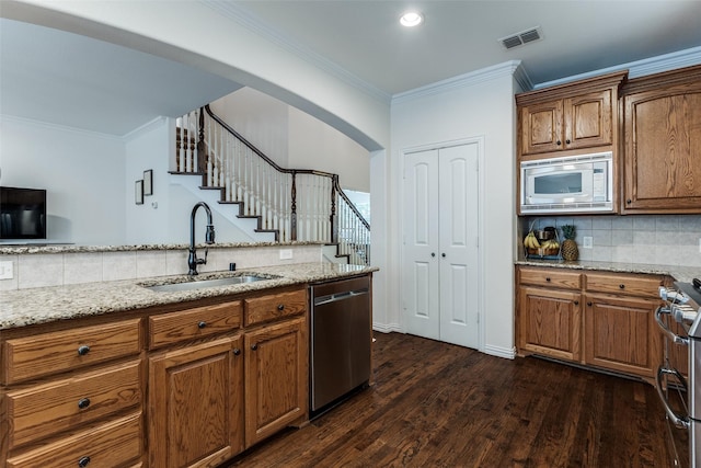 kitchen featuring appliances with stainless steel finishes, a sink, crown molding, decorative backsplash, and brown cabinets