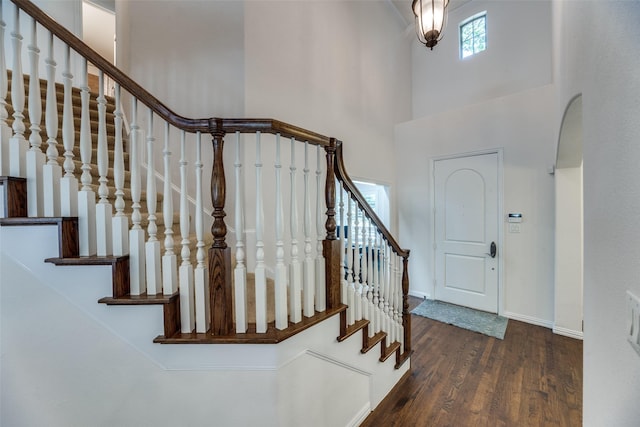 entrance foyer with wood finished floors, stairs, baseboards, arched walkways, and a towering ceiling